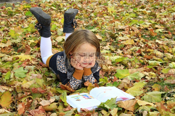年轻女孩在秋天公园读一本书躺在地上季节青少年孩子图片