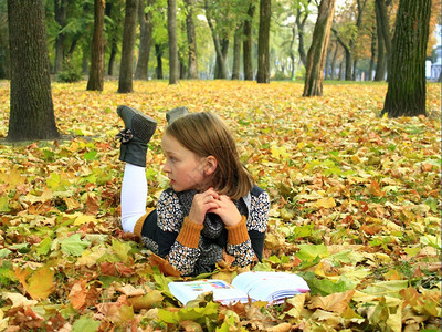 幸福老的年轻女孩在秋天公园读一本书年轻女孩在秋天公园读一本书躺在地上说谎图片