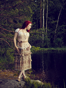 胡萝卜穿着裙子的迷人年轻女站在水线边背面湖身着洋装野池塘图片