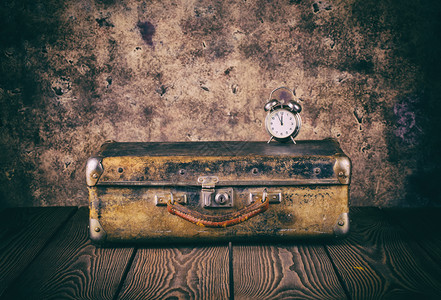皮革手提箱到达古老式木制地板加工的旧式行李箱和时钟旅行贵装李箱和木制地板上的钟概念图片