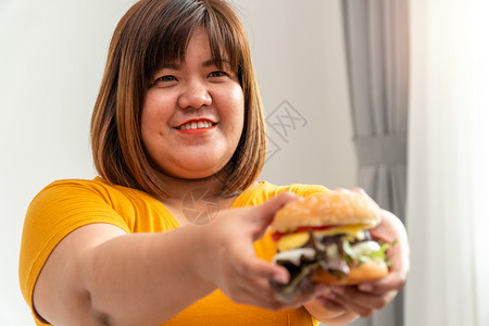 狂欢三明治饥饿的超重妇女笑着拿汉堡包坐在卧室里她非常快乐享受餐吃狂食饮紊乱症概念人们图片