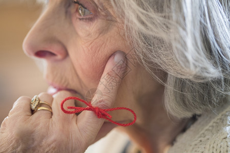 住宅退休担心用绳子绑在手指上作为提醒的高级妇女特写图片