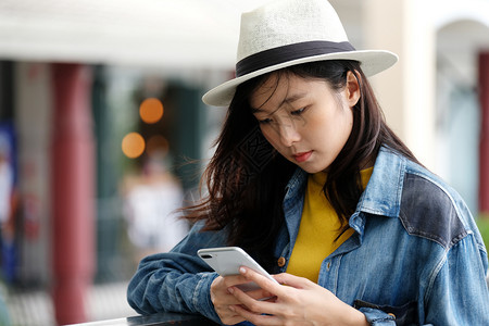 年轻亚洲女在市外咖啡馆前使用电话的年轻女他们以户外技术生活方式为背景在户外工作的人亚洲商业们图片