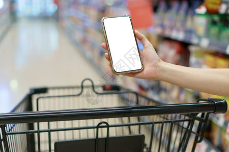 抓住Mockup双手握着空白屏幕移动电话和超市购物车数字支付概念聪明的小工具图片