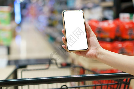 商业嘲笑Mockup双手握着空白屏幕移动电话和超市购物车数字支付概念移动的图片
