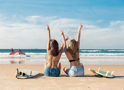两个冲浪女孩在海滩上手臂张开庆祝图片
