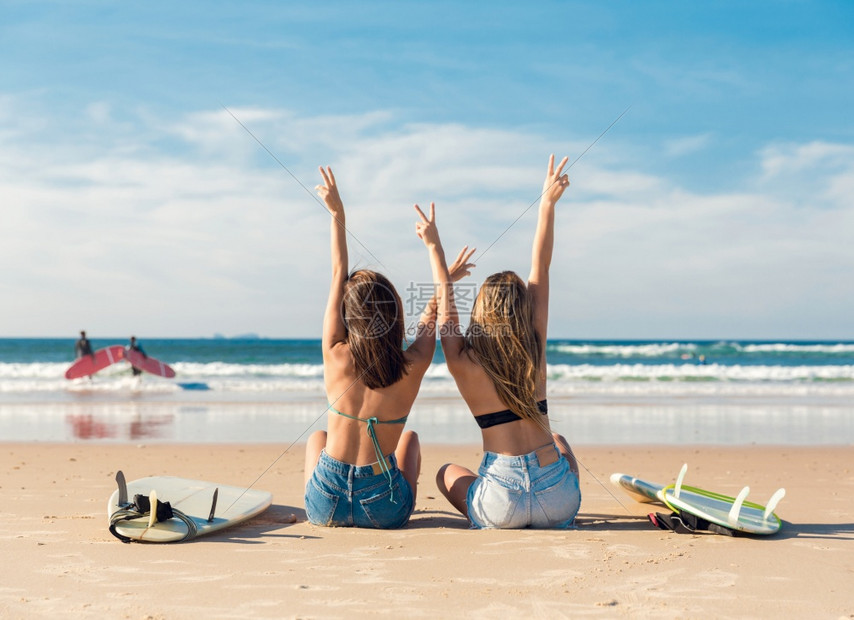 两个冲浪女孩在海滩上手臂张开庆祝图片