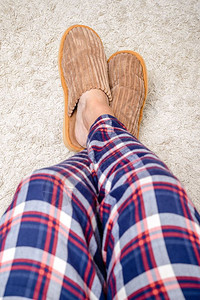 闲暇蓬松的一个有毛长腿穿暖拖鞋和睡衣的男人脚在羊毛地毯上放松屋图片