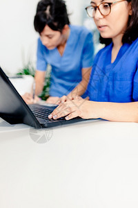 打字诊所使用笔记本电脑的女医生和护士办公室图片