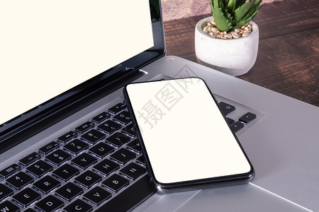 配有用品的木制桌上笔记本电脑键盘上的智能手机白空屏幕工作场所花最佳图片