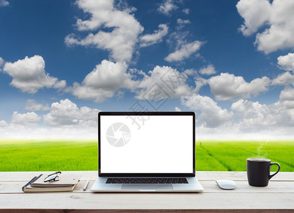 技术显示工作桌草地和蓝天空视图背景上的白屏幕膝型计算机眼镜商业图片