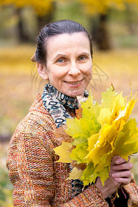 一个笑着的成年天主教女人秋在公园里采黄色的树叶橙快乐成人图片