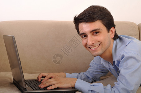人们白色的个电脑在家沙发上躺着膝型电脑的有吸引力年轻人图片
