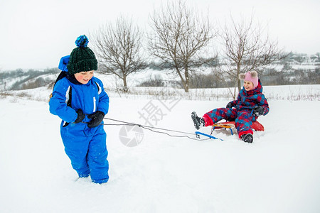 自然兄弟滑动快乐的男孩和女在冬天从山上拉雪橇冬季户外运动会寒假快乐的男孩和女在冬天从山上拉雪橇图片