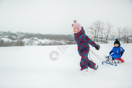 兄弟周末下雪的快乐男孩和女在冬天从山上拉雪橇冬季户外运动会寒假快乐的男孩和女在冬天从山上拉雪橇图片