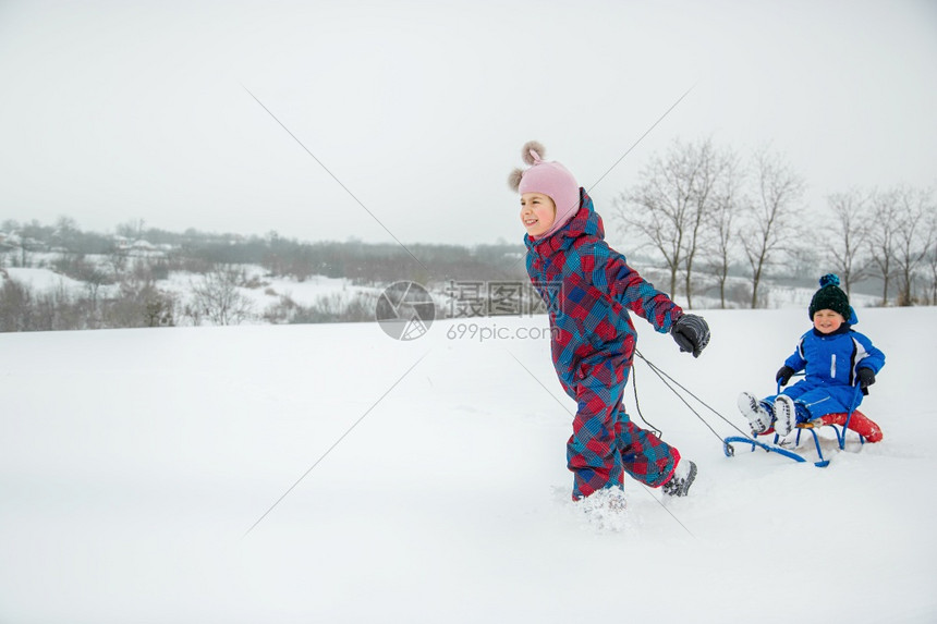 兄弟周末下雪的快乐男孩和女在冬天从山上拉雪橇冬季户外运动会寒假快乐的男孩和女在冬天从山上拉雪橇图片