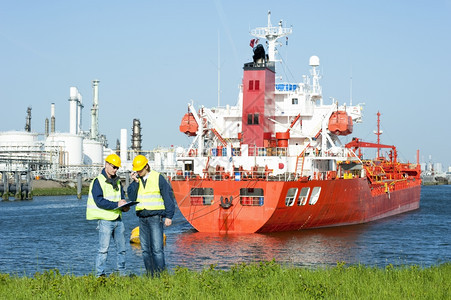 停泊白种人天线石油化学再精炼港的两名口工人戴着硬帽子和安全背心讨论对接时间表图片