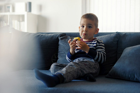 观看老的坐在沙发床上小孩拿着巧克力糖果在看电视前时手边吃着巧克力糖校对Portnoyun白种人图片