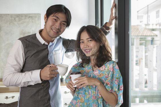 手拿着咖啡杯的亚裔年轻男女夫妇在家中客厅休息时站着放松亚洲人年轻的食物图片