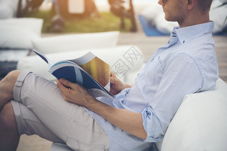 长椅高加索年轻男子阅读沙发者杂志本持有开放纸页和阅读书坐在图馆外面的沙发上露天边看书阅读男人的生活方式专业的闲暇图片