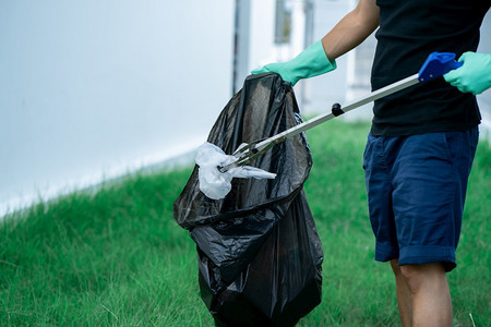 包人手使用垃圾收集设备将塑料废物存放在公园的黑袋中草绿色图片