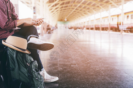 人们沟通乘客正在等待车站平台青年男子旅行者背着包和帽子在看等待火车上旅游概念的到来年轻人旅行者拿着背包和帽子期待看到亚洲图片