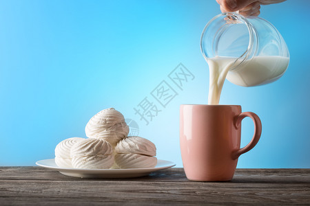 牛奶从一个罐子倒进蓝色背景的杯子健康天然食物的概念早餐牛奶从一个罐子倒进杯寒冷的盘棉花糖图片