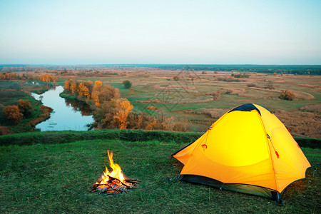 在秋季风景河上山丘陵的橙色照明帐篷和营火隐私旅行和自由的概念橙色照明帐篷和在河上山头的营火多雾路段风景优美远足图片