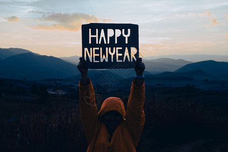 景观阳光环境手握着纸板上的新年HAPPY设计以山为背景有日落新年概念图片
