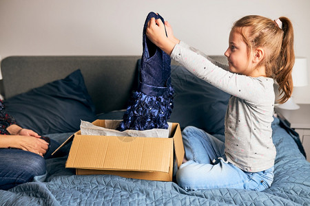母亲和女儿开箱家里有订货礼服睡在妈的沙发上在线客机顾持着裙子的送货服务时装概念包裹订购女图片