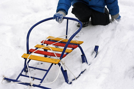 娱乐人类在冬天走户外散步的时候孩子坐在雪中他的双腿上滚动着多彩的雪橇闲暇图片
