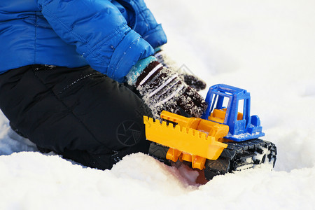 温暖的冬季儿童在雪中玩耍一个儿童坐在白雪上玩具挖土机季节霜图片