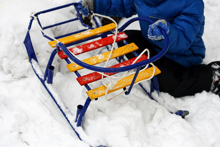 在冬天走户外散步的时候孩子坐在雪中他的双腿上滚动着多彩的雪橇新鲜卷霜图片