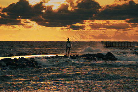 天空水太阳在暴风海的码头周围跑来去的无法辨认风筝冲浪者在戏剧橙色云层下日光照亮了落的阳光图片