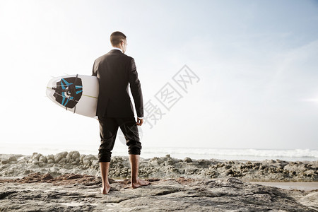 商务男士拿着冲浪板来到海边背影图片