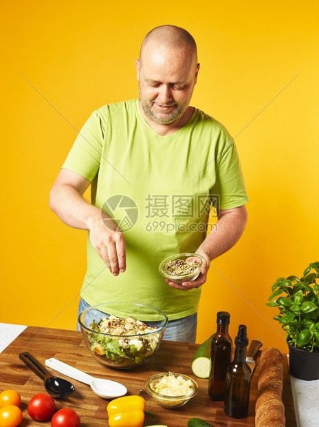 白种人关心餐桌上新鲜沙拉成分中年人撒种子黄色本底厨师图片