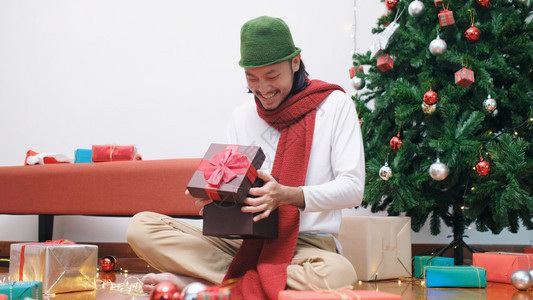 乐趣男人红色的年轻亚洲男子在圣诞节庆典晚宴上开圣诞礼物箱时带着快乐的笑容微图片