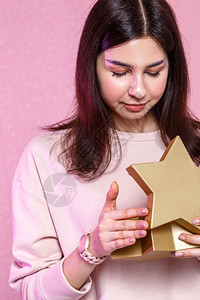 展示女金子以星形状的礼物盒在一位亚洲女孩手里一个粉红孤立背景的年轻亚洲女孩图片