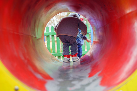 操场孩子小天主教男回到公园的观光中在游乐场上的公园里看到红隧道管中的色秋天穿着冬大衣玩得愉快地散步外套图片