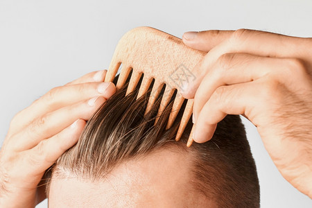 回型纹年轻的男子在家中用木梳发毛打头在家中宣传洗发圈概念宣传洗发来健康型的香波概念以及反对dandruff青年男子在家中用木梳理发纹头背景
