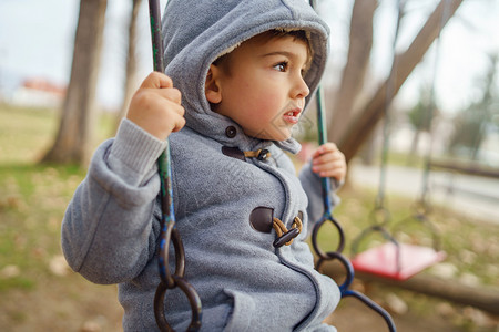 积极的一个三岁可爱小幼caucasiansian男孩的肖像冬天或秋穿大衣冬或秋在公园摇摆时戴头罩寒冷的外套图片