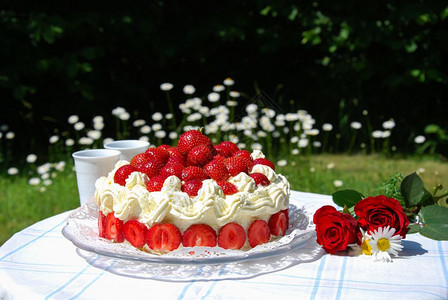 一种夏天草莓蛋糕和两个杯子在花园的桌上朵烘烤的图片