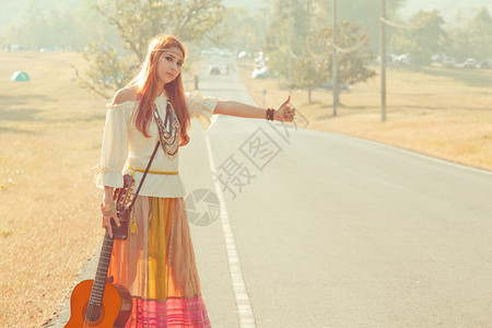 美丽的带吉他搭便车的嬉皮女孩在农村公路上运输外部图片