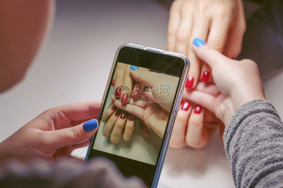 在对另一个女孩进行美容指甲修剪后不明的caucasianCaucasian女年轻在拍摄指甲油钉照片时使用智能手机为另一个女孩拍照图片