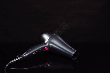 头发烘干机黑镜背景上用于美发沙龙或理店的黑色电动手持吹风机带复印空间黑镜背景上的色吹风机的图片