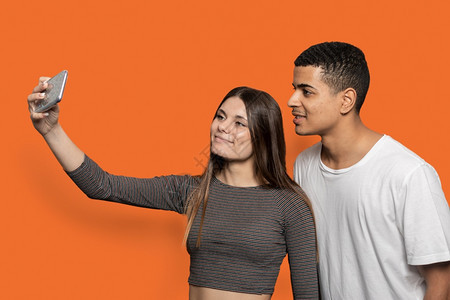水平的一对夫妇在橙色背景下用智能手机自拍的肖像朋友美国人图片