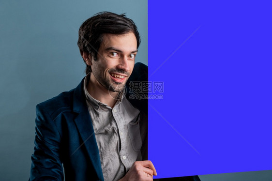 介绍信息快乐的男人拿着蓝色海报快乐微笑的年轻人展示空白招牌与的复制间区域用于标语或广告短信概念中的白种人男模常设图片