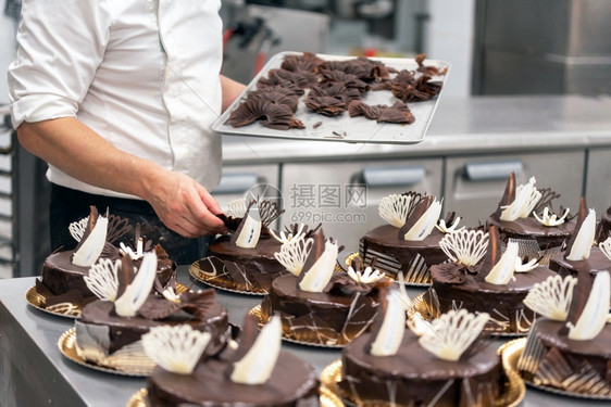 糕点师在店厨房里装饰巧克力蛋糕点师在店厨房里装饰巧克力蛋糕面包店小吃糖果图片