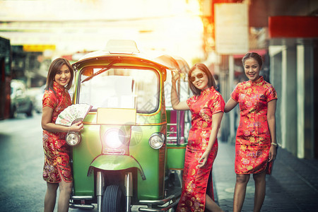 常设漂亮的微笑三名身穿传统服饰的亚洲女子站在泰国曼谷唐人街的tuktuk旁边图片