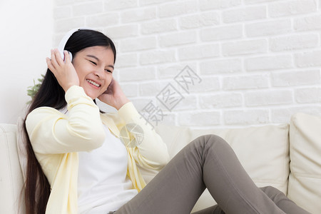 女士房间美丽的亚洲年轻女子喜欢在客厅的沙发上用耳机听音乐屋图片